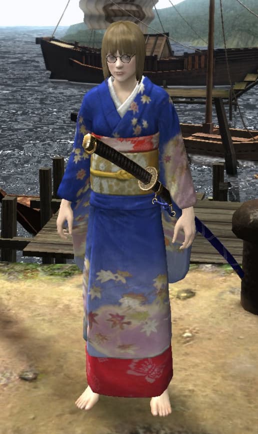 A video game character stands on a dock wearing a traditional Japanese kimono in royal blue with delicate flower patterns and a red hem. The kimono is accessorized with a decorative obi belt and a sword at the waist. The character has round glasses and shoulder-length blonde hair. In the background, wooden ships are moored at the harbor against a mountainous coastline.